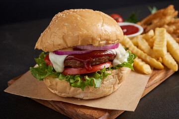 Homemade hamburger or burger with fresh vegetables and cheese lettuce and mayonnaise served, French fries on pieces of brown paper on black stone table . concept of fast food and junk food