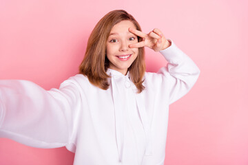 Self-portrait of attractive trendy cheerful girl showing v-sign good mood isolated over pink pastel color background