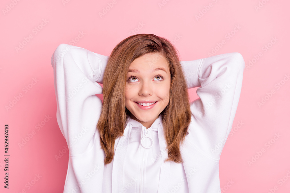 Poster Photo of shiny charming school girl wear white hoodie smiling arms behind head looking up empty space isolated pink color background