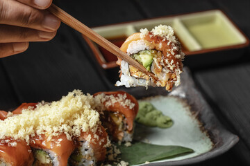 close up of chopsticks in men hands taking portion of sushi roll on the table restaurant / eating sushi roll using chopsticks