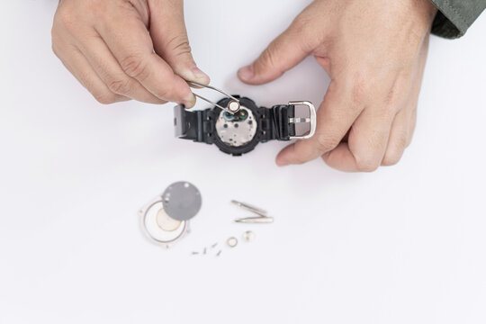A man use pliers to clamp the digital watch battery remove and change in repairing broken wristwatches on white table