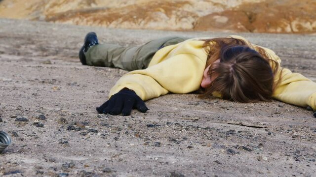 Girl exhausted from thirst lies in rocky wasteland with empty metal flask. Becoming weak hungry woman sprawled on ground. Drunk person is on sandy surface. Helplessness, early death in stone badlands