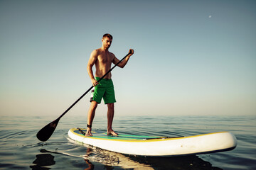 Young fit man on paddle board floating on lake.