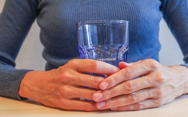 the girl is sitting at the table, holding a glass of water in her hands. Lack of vitamins in autumn and winter, uncontrolled medication, digestive problems, drinking regimen.