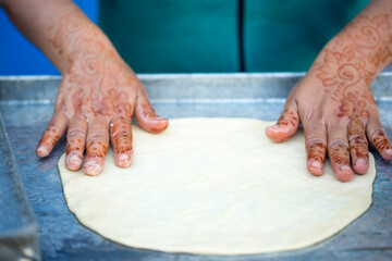 Woman with henna tattoos on hands preparing pancakes. Msemen Round flatbread dough prepared on the...