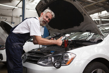 Fototapeta na wymiar Bearded elderly car mechanic repairing automobile at service station
