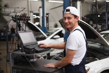 Happy car repairman smiling to the camera while running computer diagnostics for an auto
