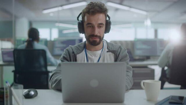 Office: Portrait of Smiling IT Programmer Wearing Headphones Working on Desktop Computer. Male Website Developer, Software Engineer Developing App, Video Game. Listening to Podcast, Music. Close-up