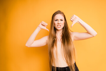 A woman with long hair, showing her thumbs up, depicts discontent on a yellow background