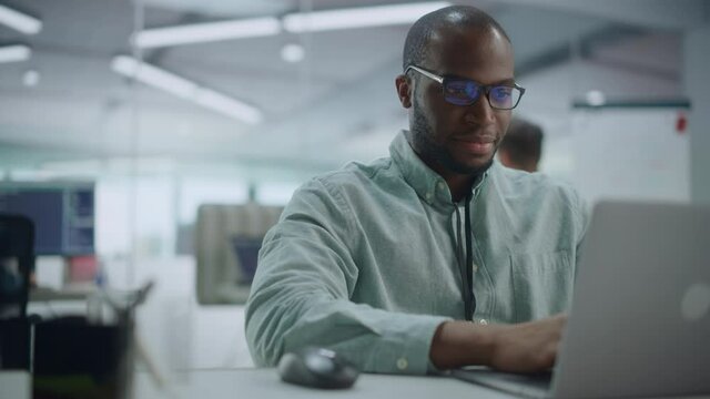 Modern Office: Portrait of Happy Black IT Programmer Working on Laptop Computer. Male Specialist Create Website, Software Engineer Develop App, Program, Video Game. Stress Free Inclusive Environment