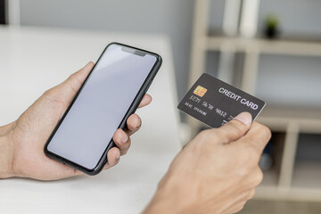 Woman holding a smartphone and a credit card, she is filling out her credit card information to pay for the purchases made through the smartphone app. Online shopping and credit card payment concept.