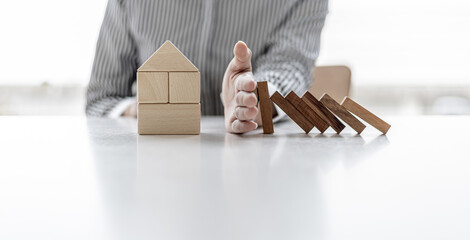 Woman using her hand to prevent wooden blocks from falling onto wooden blocks in the shape of a house, insurance to prevent risks that will save us high prices, home insurance ideas.