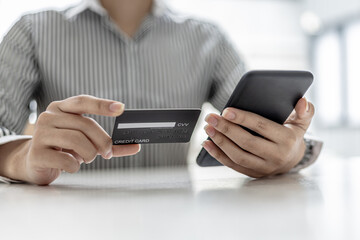 Woman holding a smartphone and a credit card, she is filling out her credit card information to pay for the purchases made through the smartphone app. Online shopping and credit card payment concept.