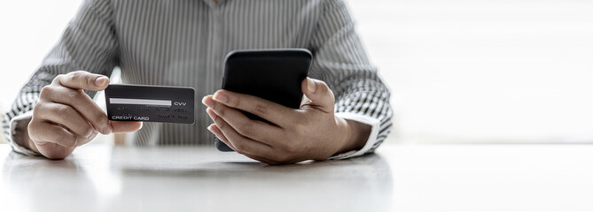 Woman holding a smartphone and a credit card, she is filling out her credit card information to pay for the purchases made through the smartphone app. Online shopping and credit card payment concept.