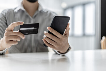 Woman holding a smartphone and a credit card, she is filling out her credit card information to pay for the purchases made through the smartphone app. Online shopping and credit card payment concept.