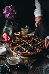 Rustic peach-blueberry-ricotta spelt pie on old wooden table served with coffee and fruits.