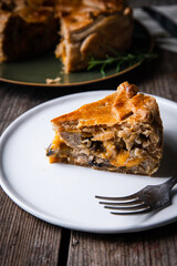 Piece of meat (sausage ), mushroom, cheddar and rosemary spelt pie decorated with crust leaves on white plate on old wooden table.