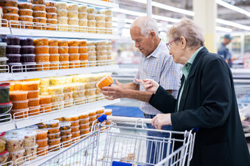 mature caucasian couple chooses pickled vegetables in the supermarket department