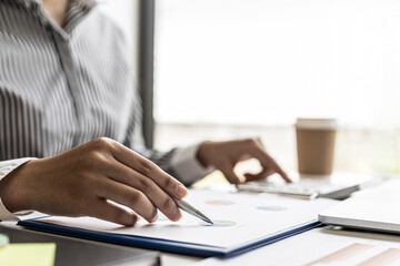 Businesswoman's hand holding a pen pointing at a bar chart on a corporate financial information sheet, the businesswoman examines the financial information provided by the finance department.