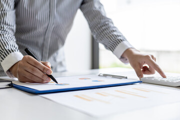 Businesswoman using a white calculator, a financial businessman examining the numerical data on a company financial document, she uses a calculator to verify the accuracy of numbers.