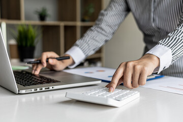Businesswoman using a white calculator, a financial businessman examining the numerical data on a company financial document, she uses a calculator to verify the accuracy of numbers.