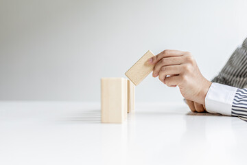 A woman is holding wooden blocks in a row, she grabs the center piece to complete them, the wooden block arrangement conveys the business operation by efficient management. Business idea.