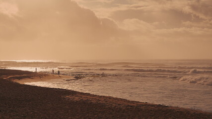 Dramatic sunrise over the ocean. Sandy coast of Oahu island, Hawaii. People walk along the beach. A ray of the sun breaks through the clouds. Sunny path along the water.