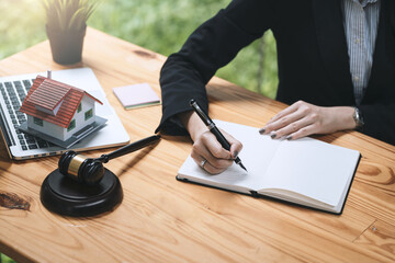 Close-up of businesswoman and lawyer hand holding pen and taking notes mallet laptop sample house...