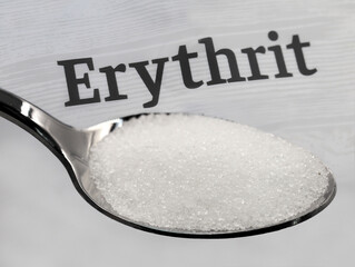 silver spoon with crystalline erythritol sugar in front of the word erythrit