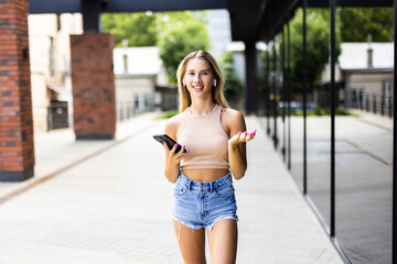 Beautiful young woman wearing jacket, carrying backpack walking outdoors, using mobile phone