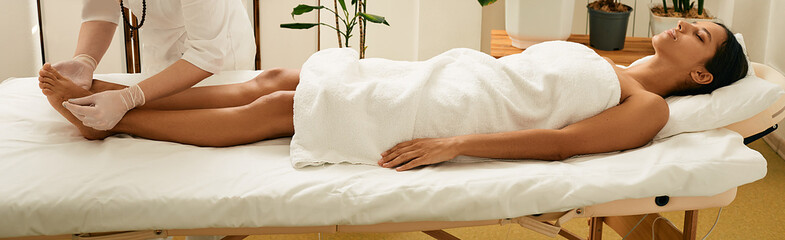 Asian woman enjoys acupuncture procedure lying on massage table at wellness spa