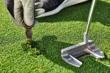 Golfer properly repair a divot mark on putting green using divot tool. Ball mark repair tool or...
