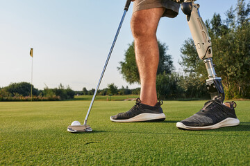 Professional golfer with prosthetic leg hitting with putter on golf ball during golfing. Concept of...