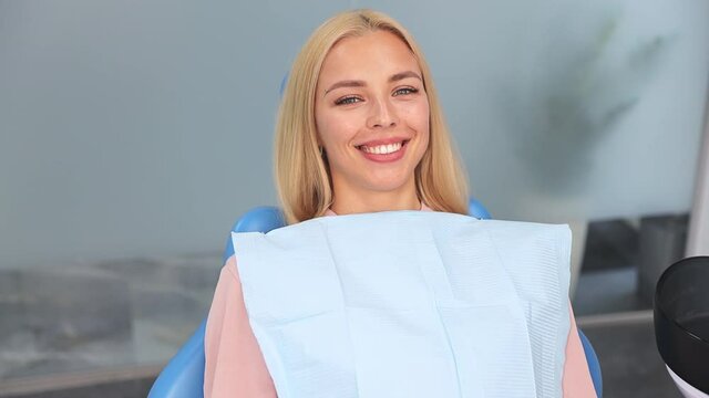 Satisfied smiling happy blonde young woman patient show okay ok gesture sitting in chair in dental clinic light office medical center with modern tools equipment. Healthy lifestyle treatment concept