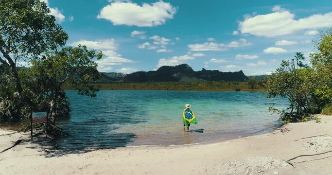 Man with Brazilian flag on a blue lake celebrating freedom.