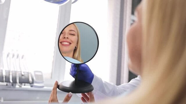 Back view male professional dentist doctor man shows mirror reflection to young satisfied woman patient dental clinic light office medical center with modern tools equipment. Healthy lifestyle concept