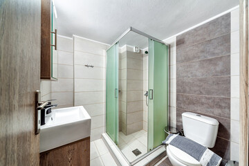 Standard modern bathroom in light colors with shower cabin built-in the corner, toilet and sink.