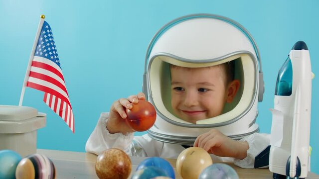 Smiling child holding a red planet Mars space rocket in his hands, close-up, pilot traveling into space. Child plays at home in an astronaut,Funny portrait little boy 5-6 years old in a toy spacesuit.