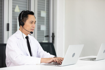 senior doctor wearing headphones and talking with patient or colleague through online video chat from laptop computer