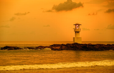 Obraz premium Panorama view of lighthouse on small rock island with orange sky and dramatic clouds at sunset. Taken in south of Thailand