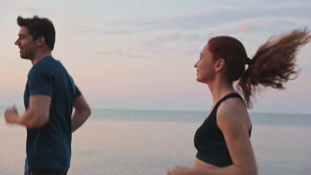 Smiling happy sporty young couple two friends family man woman together wear sports clothes warm up training running at sunrise sun dawn over sea beach outdoor on pier seaside in summer day evening