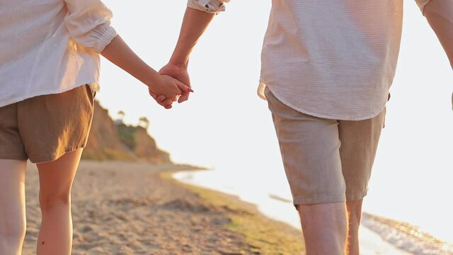 Close up cropped video young couple two friends family man woman 20s in white clothes walk go stroll hold hands together at sunrise over sea beach ocean outdoor seaside in summer day sunset evening