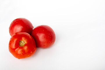 three red tomatoes on the left, on a white background