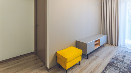 Modern interior in neutral tones. Yellow padded stool. Wooden stand.