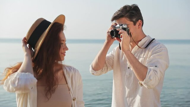 Side view young couple two friend family man woman 20s in white clothes take photo with retro vintage photo camera together at sunrise over sea beach ocean outdoor seaside in summer day sunset evening