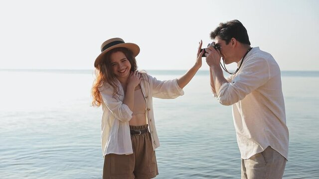 Young couple two friends family 20s in white clothes man want take photo with retro vintage photo camera woman try prevent stop at sunrise over sea beach ocean outdoor seaside in summer sunset evening