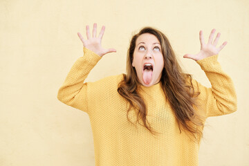 young woman with funny expression showing tongue on yellow background