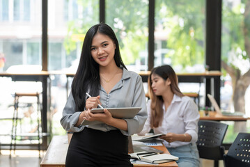 Fototapeta premium Front view of young Asian businesswoman holding a stylus tablet working. Looking at the camera.