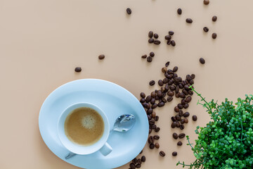 Coffeebreak with a cup of coffee, coffeebeans and green plant on beige background