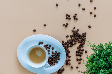 Coffeebreak with a cup of coffee, coffeebeans and green plant on beige background